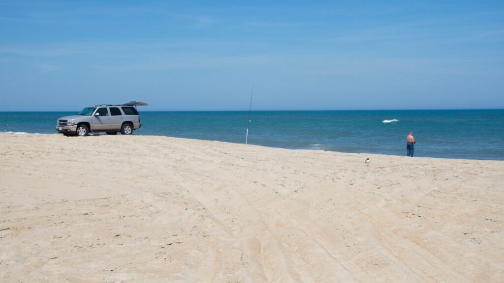 A white four-wheel-drive SUV parked on the open sand at Cape Hatteras National Seashore with the ocean beyond.