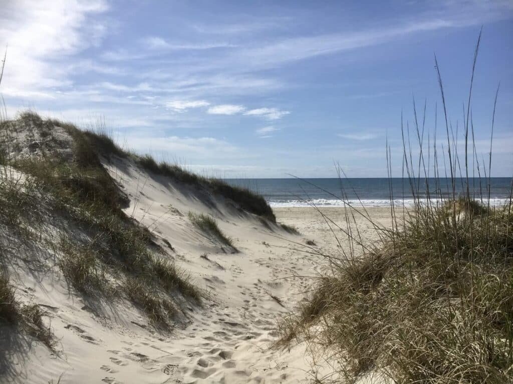 A sandy footpath cuts through sea oats and low dunes near the Ocracoke Campground under a wide sky.