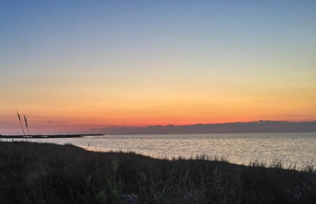 A low orange sun sets over the flat water of Pamlico Sound behind the marsh at Ocracoke.