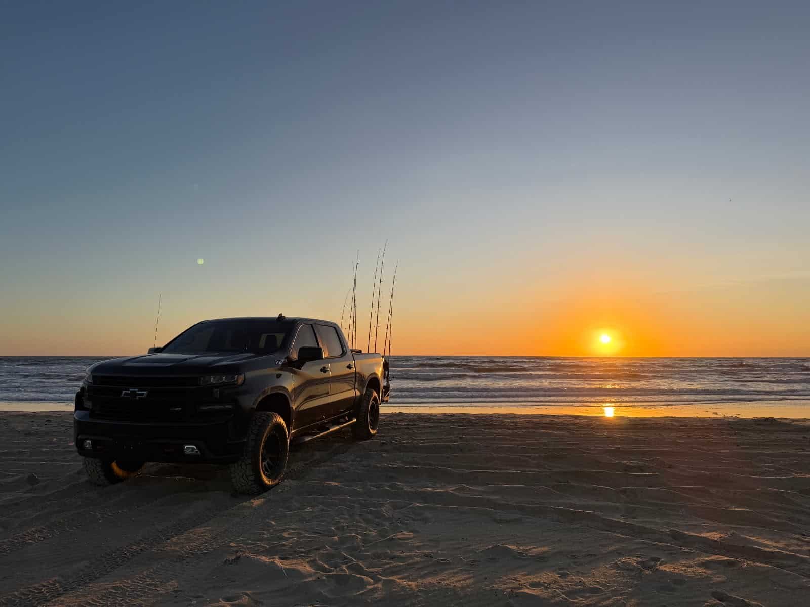 A 4x4 truck parked at sunrise on an Outer Banks beach with surf rods set