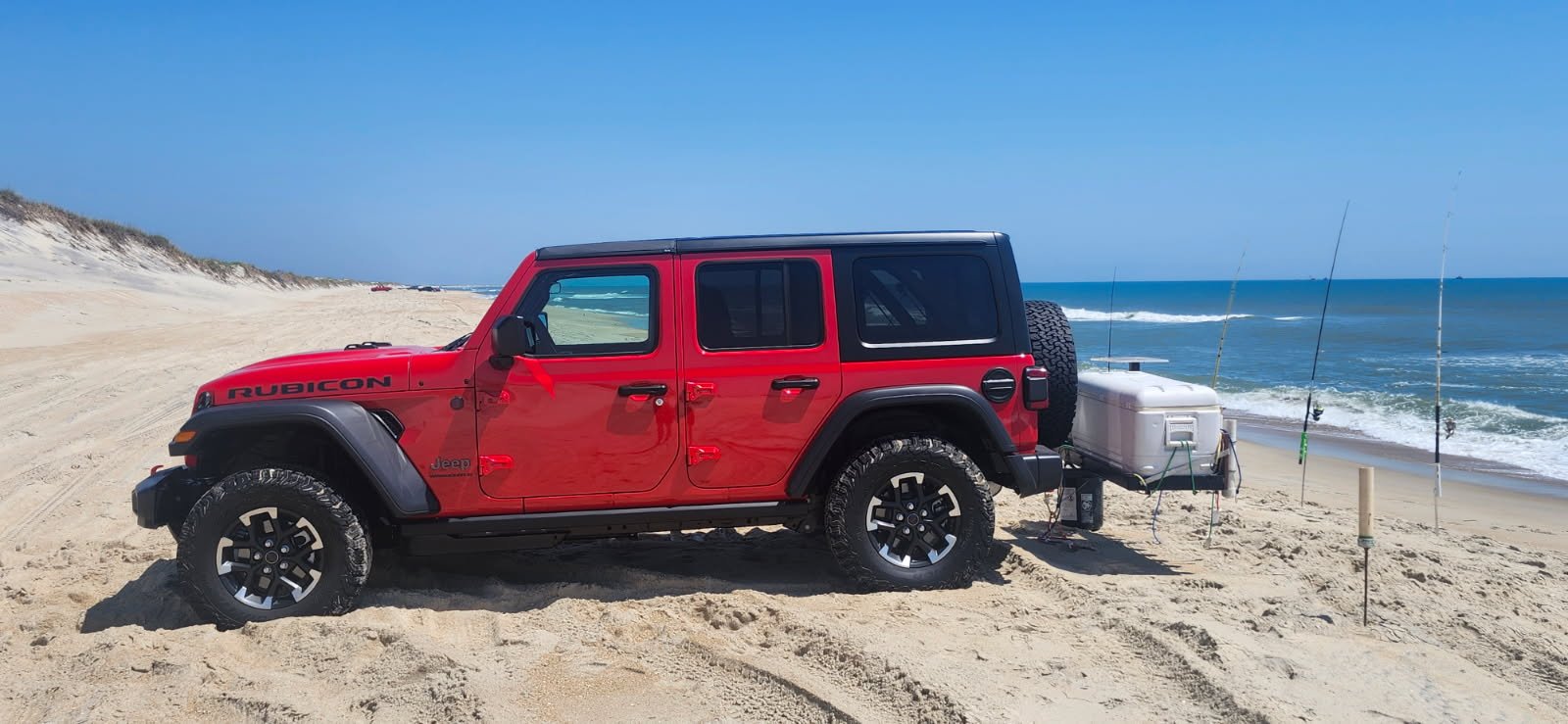 A red Jeep Wrangler Rubicon beach driving on the Outer Banks with a fishing cart