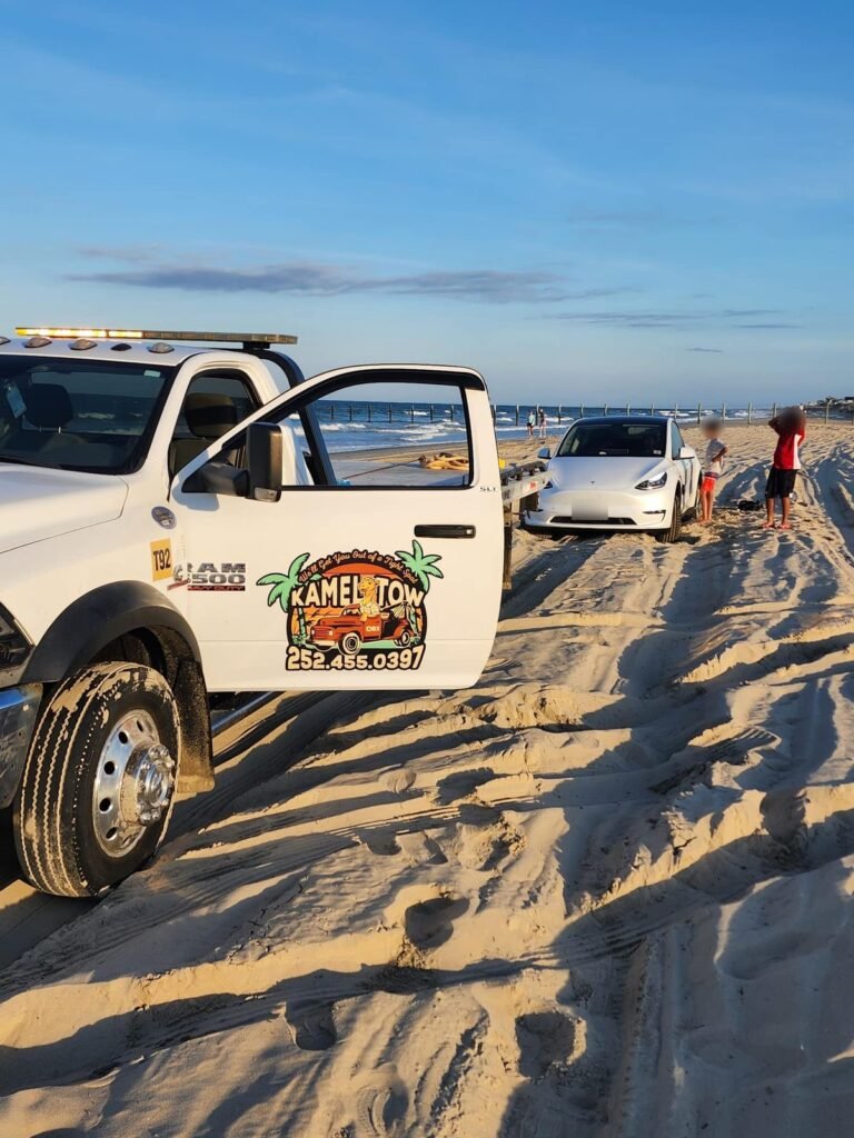 Tesla Model Y stuck in soft sand on an Outer Banks beach next to a tow truck